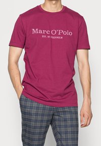 Maron farvet bomulds T-shirt med korte ærmer og rund halsudskæring, prydet med en tekstgrafik "Marc O'Polo EST. IN STOCKHOLM" i hvid.