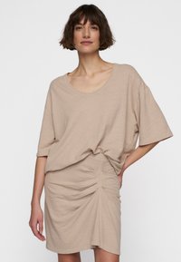 Beige t-shirt med løs pasform og bred udskæring, parret med en matchende rynket nederdel. Blødt stof, korte ærmer og subtil tekstur.
