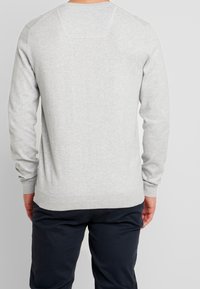 Szary sweter z dzianiny z długimi rękawami, ściągaczami przy mankietach i dolnym brzegu. Posiada klasyczny okrągły dekolt oraz subtelne detale na szwach ramion.