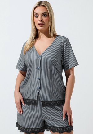 Kvinde iført grå stibet knap-op top og matchende shorts med sort blondekant, stående mod en ensfarvet baggrund.