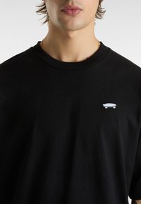 Černé bavlněné tričko s malou bílou grafikou skateboardu na levé straně hrudi. Design je jednoduchý s klasickým kulatým výstřihem.