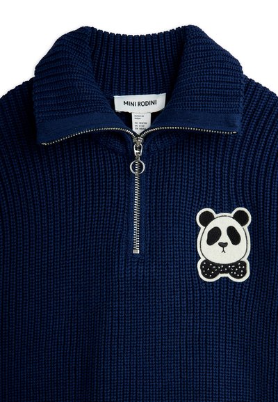 Mørk blå strikket genser med halv glidelås og metallring, med et pandaansikt-patch og sløyfe på brystet.