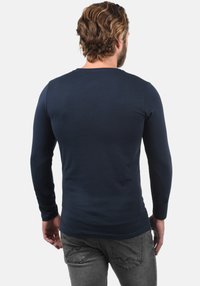 Marineblauw shirt met lange mouwen van zachte stof, met een ronde halslijn en een aansluitend model, gecombineerd met grijze spijkerbroek zichtbaar bij de taille.