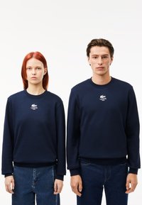 Felpe in cotone blu navy con maniche lunghe, polsini a costine e collo a giro. Presenta un piccolo logo bianco Lacoste sul petto.