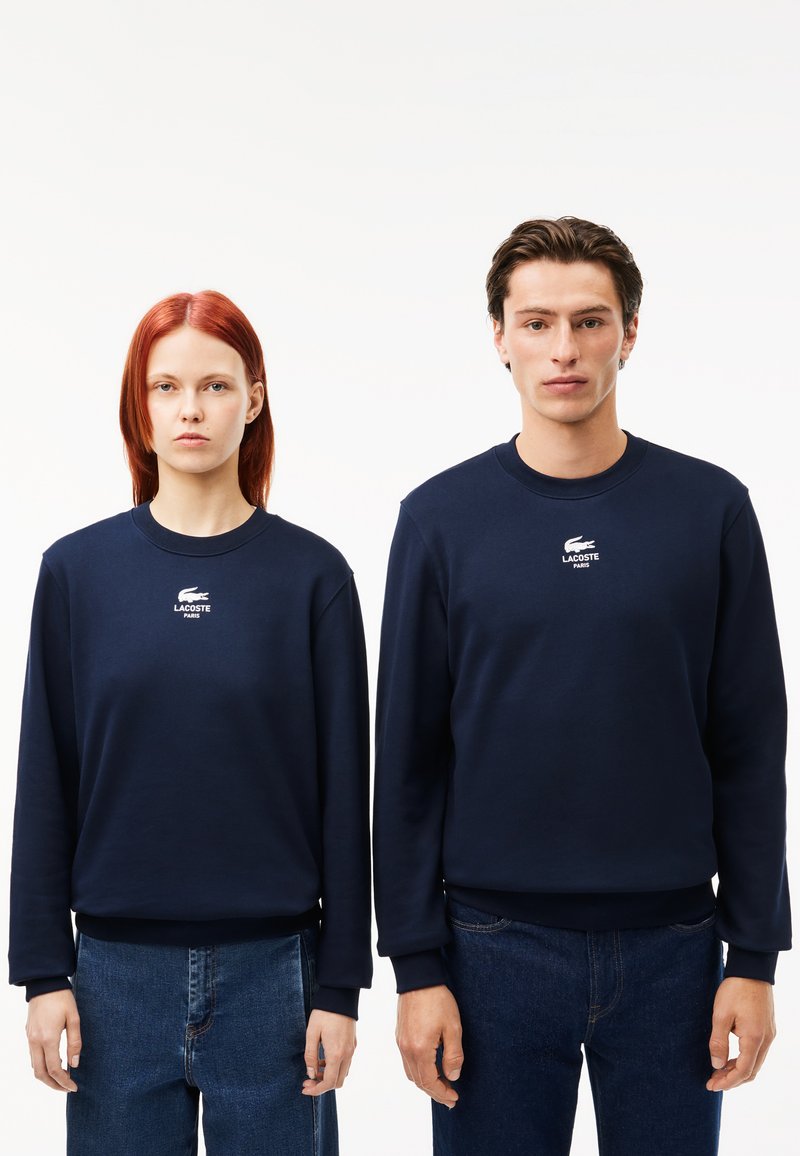 Felpe in cotone blu navy con maniche lunghe, polsini a costine e collo a giro. Presenta un piccolo logo bianco Lacoste sul petto.