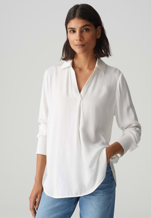 White long-sleeve blouse with a v-neckline and buttoned cuffs, made from a smooth, lightweight fabric, featuring a relaxed fit and side slits.