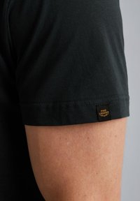 Čierna polokošeľa s krátkym rukávom vyrobená z bavlny. Má prešívaný lem a malú značkovú etiketu na rukáve. Hladká textúra.