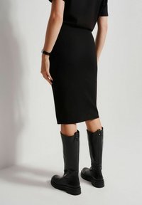 Czarna, dopasowana spódnica midi w połączeniu z czarnymi, skórzanymi botkami sięgającymi za kolano, charakteryzującymi się gładką teksturą i wyraźnymi zamkami na plecach.