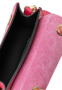 Borsa a tracolla in suede rosa e pelle lucida con interno nero, caratterizzata da accessori dorati e una forma strutturata e cilindrica.