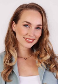 Schwarze V-förmige Halskette an einer Frau mit welligem, blonden Haar, die eine hellblaue Jacke und ein weißes Oberteil trägt, lächelnd vor einem neutralen Hintergrund.