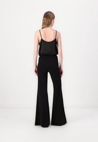 Svart ermeløs topp kombinert med høyhalsede svarte vide bukser. Glatt stoff med minimalistisk design, ingen synlige mønstre eller maskinvare.