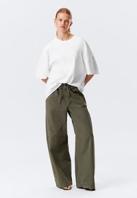 T-shirt bianco oversize in cotone, abbinato a pantaloni larghi verde oliva con vita regolabile e gambe larghe.