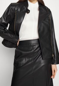 Black leather motorcycle jacket with zippered closure, no collar, and matching black leather skirt. Smooth texture, fitted design.