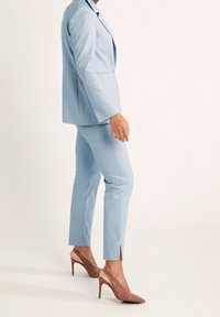 Ljusblå skräddarsydd kostym med en enkelskärmad jacka och slim-fit byxor, kombinerat med tan högklackade skor. Slät textur, elegant design.