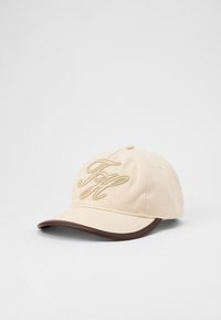 Beige baseball cap with brown brim edge and embroidered stylized initials on front, displayed on a plain white background.
