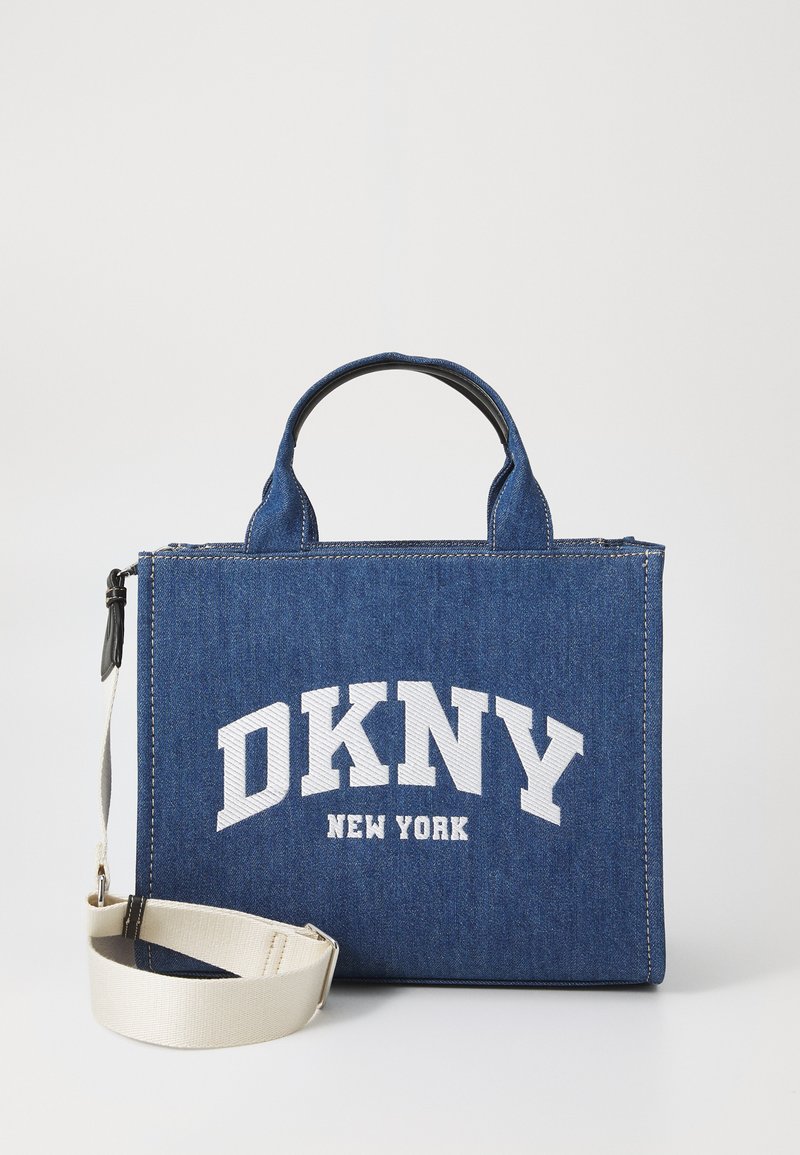Džinsinė rankinė, turinti stačiakampio formą, dvi rankenas ir reguliuojamą kremozinės spalvos diržą. Priekyje yra užrašas „DKNY NEW YORK“ balta spalva.