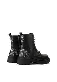 Stivali da combattimento neri realizzati in pelle liscia con accenti in tessuto a motivo. Chiusura con lacci davanti e zip laterale, suola in gomma spessa.