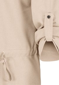 Beige textured fabric with a tied waist and rolled sleeve. Features a snap button on the cuff and subtle stitching details.