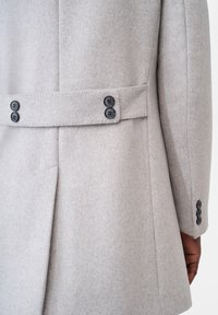 Cappotto di lana grigio chiaro con un design aderente, doppio petto, bottoni neri e dettaglio della cintura in vita.