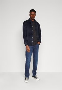 Cămașă flanelată în carouri bleumarin, purtată deasupra unui tricou negru, asortată cu blugi și adidași negri. Design cu nasturi, textură netedă.