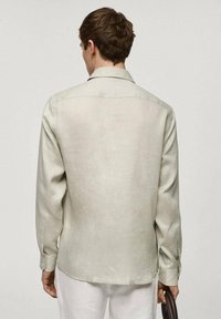 Camicia verde chiaro a maniche lunghe con un tessuto liscio e testurizzato. Presenta un colletto, polsini con bottoni e un orlo curvo. Vista posteriore.