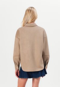Beige suède shirt met een kraag, verlaagde schouders en knoopmanchetten. Draag het met een donkere spijkerrok. Gladde textuur, casual pasvorm.