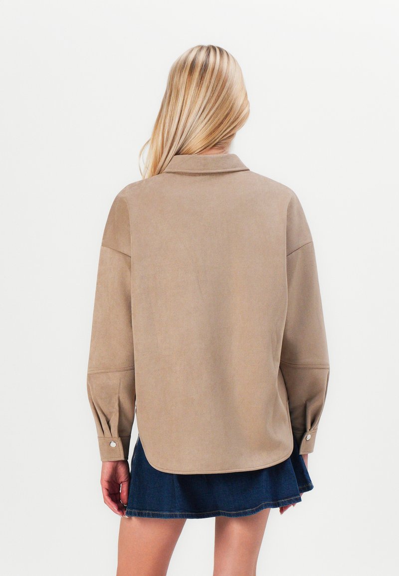 Camicia in suede beige con colletto, spalle scese e polsini abbottonati. Indossata con una gonna in denim scuro. Texture liscia, vestibilità casual.