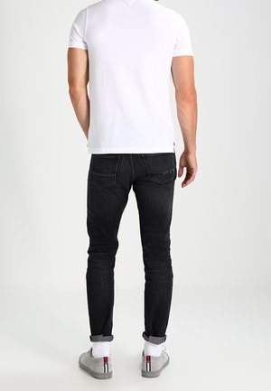 Slim-fit svarta jeans med fem fickor, uppvikta ben och kontrasterande sömmar. Kombinerat med en enkel vit t-shirt med kort ärm och grå sneakers.
