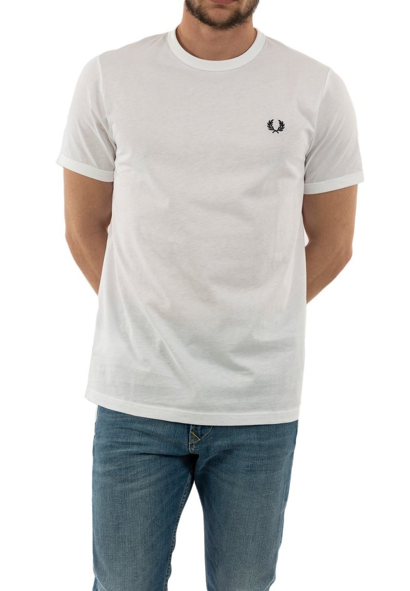 Camiseta blanca de algodón de mangas cortas, con cuello de canalé en contraste y logo bordado en el lado izquierdo del pecho. Combinada con jeans azules.