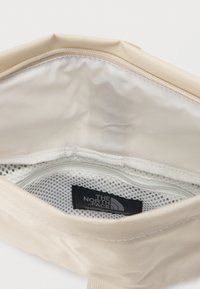 Μπεζ υφασμάτινη θήκη με ανοικτό φερμουάρ που αποκαλύπτει εσωτερική τσέπη από λευκό δίχτυ και μαύρη ετικέτα The North Face.