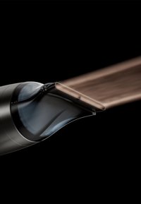 Gros plan sur une buse de sèche-cheveux noire émettant un jet concentré d'air chaud sur un fond noir.