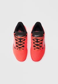 Ζευγάρι φωτεινά κοραλλί αθλητικά παπούτσια με μαύρη γλώσσα, κοραλλί κορδόνια και λευκό λογότυπο, σε θέα από πάνω σε ανοιχτό φόντο.