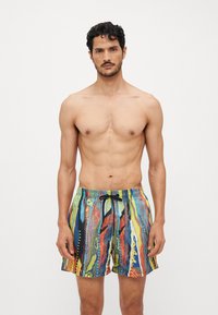 Shorts de bain colorés avec taille élastique à cordon de serrage, présentant un motif abstrait en vagues de bleu, rouge, jaune et vert sur un tissu léger.