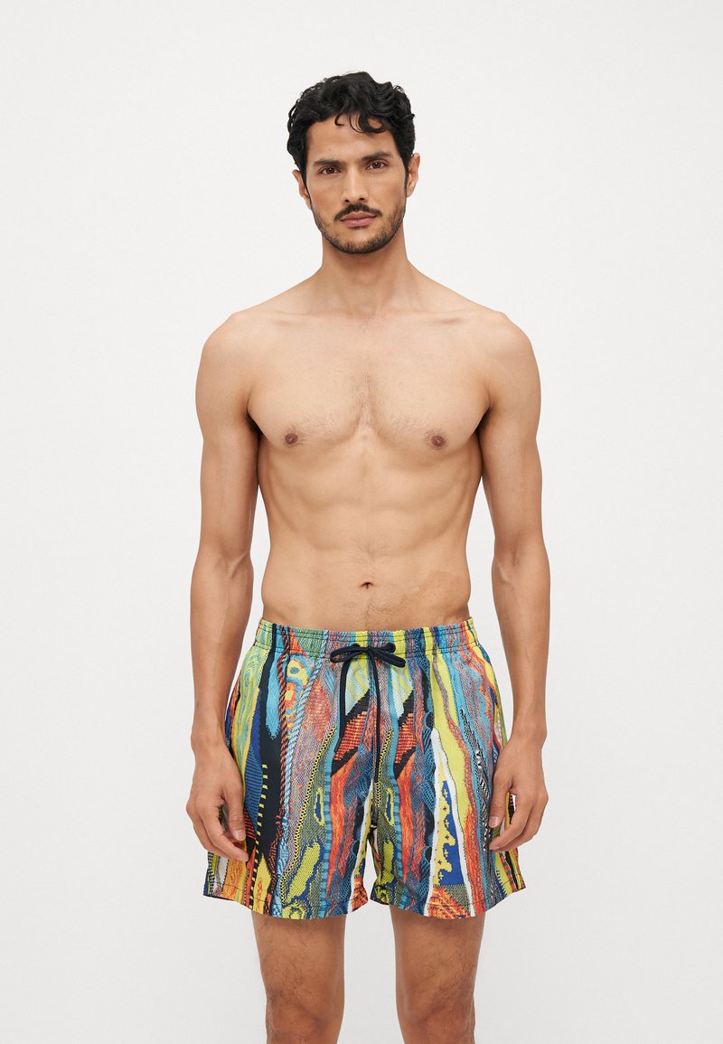 Shorts de bain colorés avec taille élastique à cordon de serrage, présentant un motif abstrait en vagues de bleu, rouge, jaune et vert sur un tissu léger.