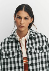 Sort-hvidternet jakke med krave, der har to forlommer og sorte knapper over et stribet, flerfarvet inderlag.