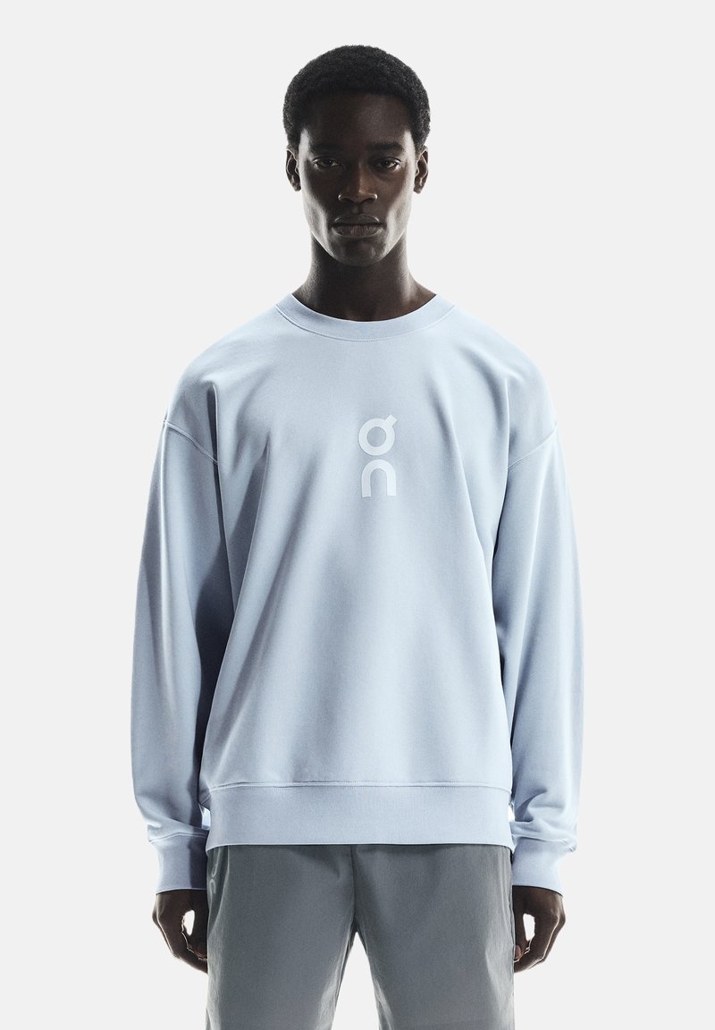 Lichtblauwe sweatshirt met een ronde hals, ontspannen pasvorm en een wit logo in het midden. De stof lijkt glad met ribgebreide boorden en onderrand.