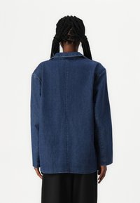 Temno pranje jeans jakna s sproščenim krojem, ovratnikom in dolgimi rokavi. Ima ravno hrbtno šiv in minimalističen dizajn.