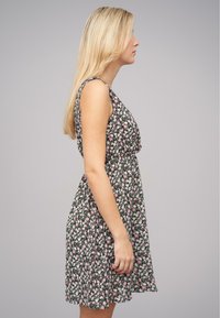 Robe florale avec un fond noir, ornée de fleurs roses et blanches, sans manches, avec un haut ajusté et une jupe évasée.