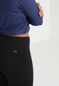 Czarne legginsy o wysokim stanie z boczną kieszenią na zamek, zestawione z dopasowaną granatową bluzką z długim rękawem z teksturowanym wzorem.
