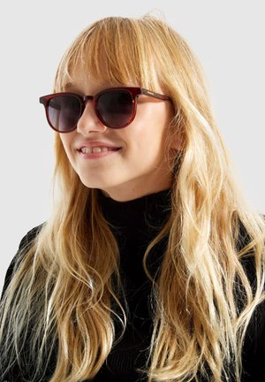 Tortoiseshell zonnebril met donkere lenzen, ronde monturen en een gestroomlijnd ontwerp, gedragen door een model met lang, golvend blond haar.