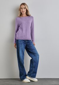 Maglione lavorato a maglia color lavanda con maniche lunghe, scollo rotondo, abbinato a jeans blu in denim larghi e scarpe da ginnastica bianche. Texture liscia, design casual.