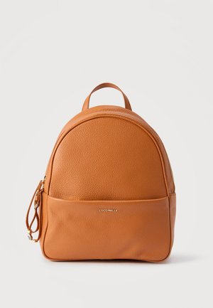 Liten ryggsekk i lyst skinn med topphåndtak, frontlomme med glidelås og gyllen "Coccinelle"-logo på glatt og kornet tekstur.