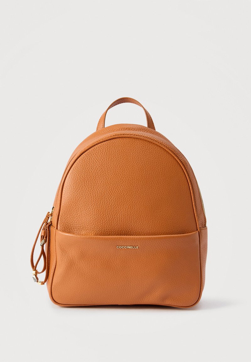 Μικρό μπεζ δερμάτινο σακίδιο με χειρολαβή στην κορυφή, μπροστινή τσέπη με φερμουάρ και το χρυσό λογότυπο "Coccinelle" πάνω σε λείες και ανάγλυφες υφές.