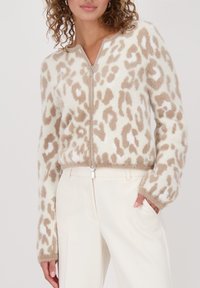 Flauschiger Reißverschluss-Pullover in Creme mit beigefarbenem Leopardenmuster. Mit langen Ärmeln und weichem Material, kombiniert mit weißen Hosen.