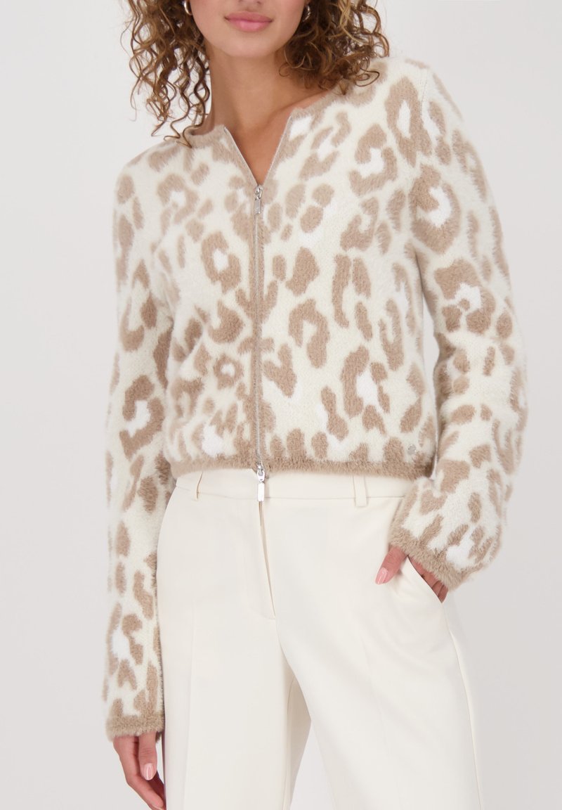 Flauschiger Reißverschluss-Pullover in Creme mit beigefarbenem Leopardenmuster. Mit langen Ärmeln und weichem Material, kombiniert mit weißen Hosen.