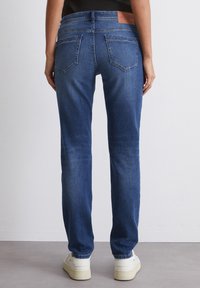 Blå denim jeans med rette ben, med baklommer og en merket skinnlapp i midjen. Lette slitasjemerker synlige.