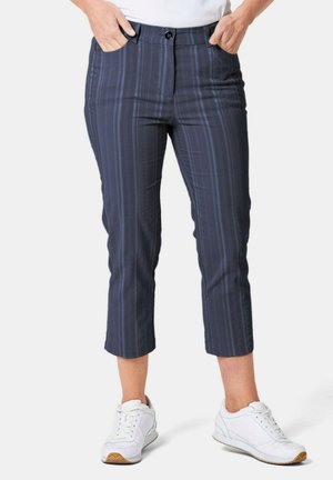 Marineblauwe cropped broek met verticale strepen. Gemaakt van een gladde stof, heeft voorzakken en een knoopsluiting. Gepaard met witte sneakers.