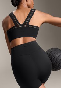 Black athletic sports bra with a V-shaped back and cut-out details, paired with high-waisted black shorts. Textured rubber ball in background.