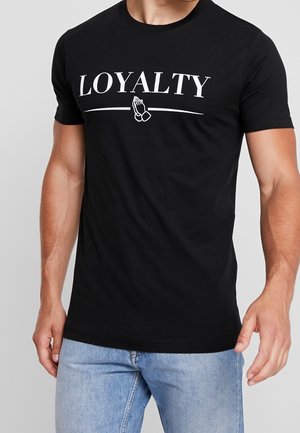 Camiseta negra de algodón con la palabra "LEALTAD" en blanco, junto con un gráfico de manos en oración debajo, manga corta y cuello redondo.