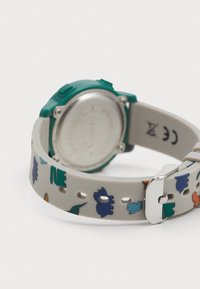 Montre en silicone avec un boîtier vert et un bracelet blanc orné de motifs de dinosaures colorés. Quincaillerie en argent et dos métallique lisse.